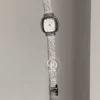 A delicate blend of modern elegance and vintage charm, this silver sparkle oval women's watch is designed to make a subtle yet striking statement. Featuring a polished oval case and a minimalist white dial, the design is elevated by a shimmering textured strap that catches the light beautifully with every movement.