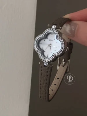Bring a distinctive touch to your everyday style with this GEDI women's watch. A clover-shaped case with a decorative beaded border frames a softly shimmering dial, combining playful curves with classic elegance. The polished silver-tone finish contrasts beautifully with the slim, textured strap and its neat stitching. Simple hour markers keep the design balanced, making this watch an elegant finishing touch for relaxed outfits, office looks, or weekend occasions.